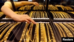 FILE - An employee arranges gold jewelry in a display case as her arm is reflected in the mirror, at a gold shop in Wuhan, Hubei province, Aug. 25, 2011. 