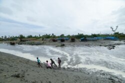 Orang-orang desa berjalan melewati pantai saat air laut menyembur setelah memecahkan tanggul di pantai Teluk Bengal di 24 pargana Selatan, negara bagian Benggala Barat, India, Selasa, 25 Mei 2021. Sekitar 10 ribu orang dievakuasi karena badai Yaas. (Foto: AP)