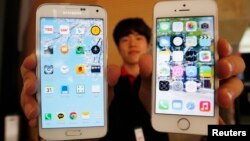 Seorang pegawai toko di Seoul memegang ponsel Samsung Electronics edisi Galaxy 5 (kiri) dan Apple Inc seri iPhone 5. (Foto: Dok)