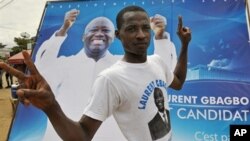 A supporter poses by a poster of Ivory Coast President Laurent Gbagbo in Abidjan, 16 Oct 2009