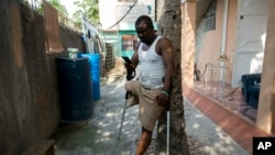 FILE - Amputee and prosthetic technician Wilfrid Macena leans against a tree in his yard as he looks at his smart phone, in Carrefour, Haiti, June 5, 2019. 