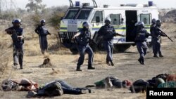Policías observan los cadáveres de mineros sudafricanos, víctimas fatales de un enfrentamiento con la policía.