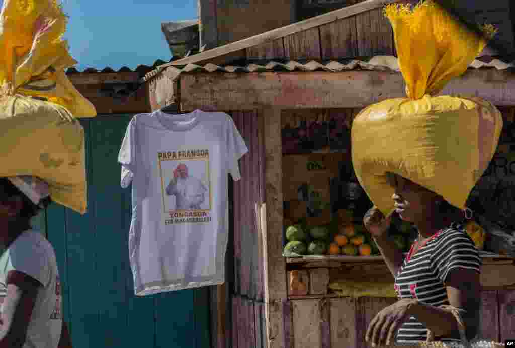 Women carrying bags on their heads pass a stall selling T-shirts of Pope Francis ahead of his visit to Madagascar next weekend, in Antananarivo, Madagascar.