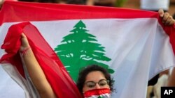 FILE - An anti-government protester shouts slogans while wearing a mask with the colors of the Lebanese flag in Beirut, Lebanon, July 2, 2020. 