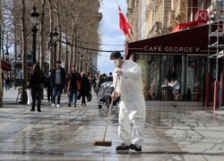 A masked worker wipes the pavement of the Champs Elysees avenue in Paris, March 13, 2020.