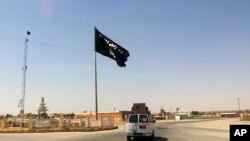 ARCHIVES - Un véhicule passe devant un drapeau du groupe État islamique dans le centre de Rawah, à 281 kilomètres au nord-ouest de Bagdad, en Irak, le 22 juillet 2014. 