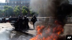 Des policiers anti-émeute devant une voiture renversée lors d'une manifestation des chauffeurs de taxi, le jeudi 25 Juin, 2015 Paris, France.