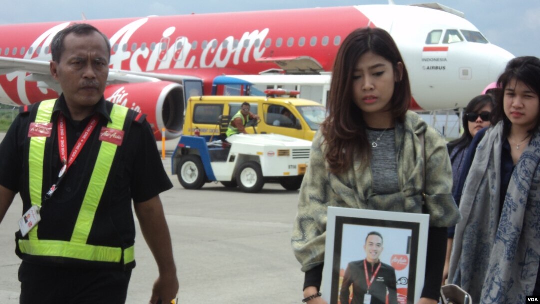 Kerabat Oscar Desano membawa fotonya di depan pesawat AirAsia yang membawa jenazah pramugara maskapai tersebut di Bandara Adi Sumarmo, Solo (14/1). (VOA/Yudha Satriawan)