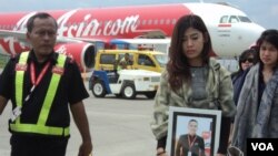 Kerabat Oscar Desano membawa fotonya di depan pesawat AirAsia yang membawa jenazah pramugara maskapai tersebut di Bandara Adi Sumarmo, Solo (14/1). (VOA/Yudha Satriawan)