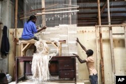 FILE - Manager of Texfad, John Baptist Okello, right,speaks to an employee as she weaves a carpet using banana fibre threads, at the Texfad factory in Sonde, Mukono District, Uganda, Sept. 20 2023.