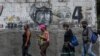 Ciudadanos con mascarillas pasan frente a un mural que representa al fallecido presidente venezolano Hugo Chávez en el centro de Caracas. Agosto 25, 2020.