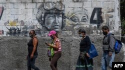 Ciudadanos con mascarillas pasan frente a un mural que representa al fallecido presidente venezolano Hugo Chávez en el centro de Caracas. Agosto 25, 2020.