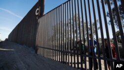 Boys look through an older section of the border structure from Mexicali, Mexico, alongside a newly constructed, taller section, left, in Calexico, Calif., March 5, 2018. President Trump tweeted about new work on the border wall, but this work began in February and wasn't funded by the budget he just signed.