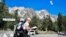 A hiker looks at a map as he walks in a parking lot beneath the Planpincieux glacier, seen at background right, in the Alps on the Grande Jorasses peak of the Mont Blanc massif, in Val Ferret, near Courmayeur, northern Italy, Aug. 7, 2020.