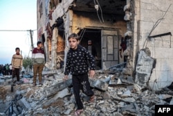 People walk through the rubble of a building heavily damaged by Israeli bombardment, in Rafah in the southern Gaza Strip on February 11, 2024, amid the ongoing conflict between Israel and the Palestinian militant group Hamas. (Photo by SAID KHATIB / AFP)