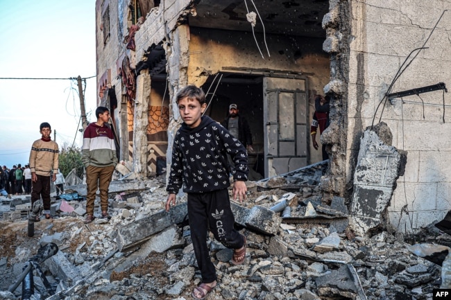 People walk through the rubble of a building heavily damaged by Israeli bombardment, in Rafah in the southern Gaza Strip on February 11, 2024, amid the ongoing conflict between Israel and the Palestinian militant group Hamas. (Photo by SAID KHATIB / AFP)