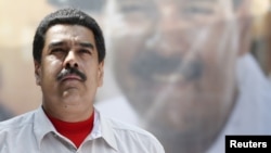 FILE - Venezuela's President Nicolas Maduro stands in front of a picture of himself during a meeting with government workers in Caracas.