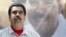 FILE - Venezuela's President Nicolas Maduro stands in front of a picture of himself during a meeting with government workers in Caracas.