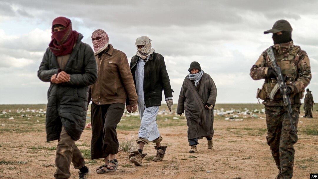 Men suspected of being an Islamic State (IS) group's fighter walk next to a member of the Kurdish-led Syrian Democratic Forces (SDF) as they wait to be searched after leaving the IS group's last holdout of Baghouz, Syria, Feb. 27, 2019.