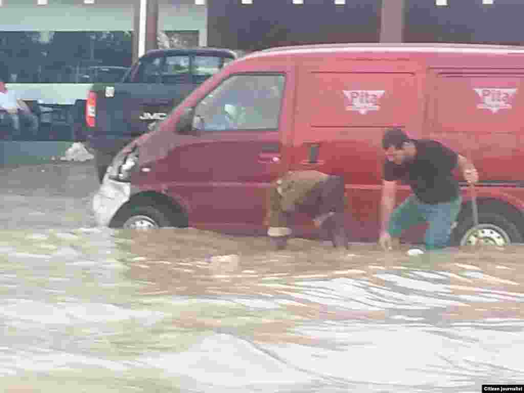 Dois senhores à volta de um carro preso numa estrada inundada em Luanda