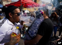 José Luis Candanosa sopla humo de cigarro sobre "La Santa Muerte", por la creencia de que éste la puede purificar, en el barrio de Tepito de la Ciudad de México, el martes 1 de noviembre de 2022.