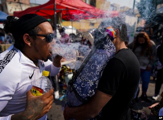 José Luis Candanosa sopla humo de cigarro sobre "La Santa Muerte", por la creencia de que éste la puede purificar, en el barrio de Tepito de la Ciudad de México, el martes 1 de noviembre de 2022.