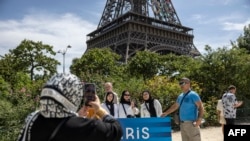 FILE - Tourists pose in front of the Eiffel Tower in the background in Paris on August 4, 2024, during the Paris 2024 Olympics games. 