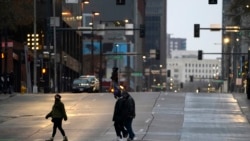 Pedestrians wear masks while crossing an empty road at the intersection of Market Street and 15th Avenue during the evening rush hour Monday, Dec. 28, 2020, in downtown Denver. (AP Photo/David Zalubowski)