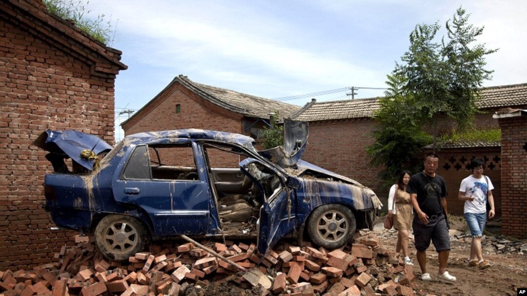 Chinese people walk past a flood-damaged vehicle sitting on the bricks at a village in Fangshan district of Beijing, China, July 23, 2012. 
