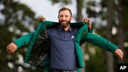 FILE - Tiger Woods helps Masters champion Dustin Johnson with his green jacket after his victory at the Masters golf tournament, Nov. 15, 2020, in Augusta, Ga.