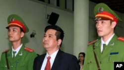 Cu Huy Ha Vu stands between policemen in front of the dock during his trial at a court in Hanoi, April 4, 2011.