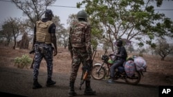 FILE - A police officer and a soldier from Benin stop a motorcyclist at a checkpoint outside Porga, Benin, March 26, 2022.