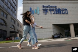 FILE - Women wearing masks to prevent the spread of the coronavirus chat as they pass by the headquarters of ByteDance, owners of TikTok, in Beijing, China, Aug. 7, 2020.
