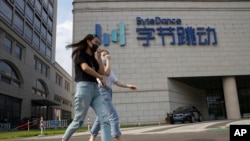 FILE - Women wearing masks to prevent the spread of the coronavirus chat as they pass by the headquarters of ByteDance, owners of TikTok, in Beijing, China, Aug. 7, 2020.