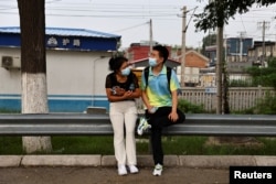 Zu Wenbao, 23, and his mother Zhao Guorong, 59, wait for a bus on the way to the music studio of 38-year-old music teacher Chen Shensi, for a practice session with members of Zu's band Star Kids, who like him are all adults with autism spectrum disorder, in Beijing, China August 21, 2022. (REUTERS/Tingshu Wang)