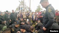 Policías sentados mientras funcionarios de la Defensoría del Pueblo de Colombia hablan con manifestantes que, según las autoridades, exigen que la petrolera Emerald Energy construya carreteras en San Vicente del Caguán, Colombia, el 2 de marzo de 2023.