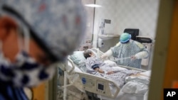 FILE - A physician stands outside a room at an Intensive Care Unit as a nurse suctions the lungs of a COVID-19 patient, April 20, 2020, in Yonkers, New York.