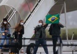 Brazilians hold a Brazilian flag after arriving from Wuhan, China, the epicenter of the coronavirus at the Annapolis Air Force Base, in Anapolis city, Goias state, Brazil, Feb. 9, 2020.