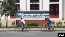 Two cyclists are seen riding past the University of Health Sciences, on 8 August 2015. (Photo: Ouch Nida/VOA Khmer)