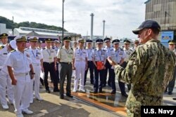 FILE - In this photo by U.S. Navy, Capt. Brett E. Crozier, commanding officer of the U.S. 7th Fleet flagship USS Blue Ridge (LCC 19), welcomes members of the Japan Self-Defense Force Joint Staff College for a tour aboard the ship, Sept. 18, 2018.