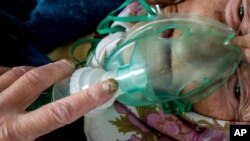FILE - An elderly woman suffering from COVID-19 breathes with the help of an oxygen mask in a hospital in Pochaiv, Ukraine, May 1, 2020. 
