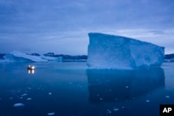 Sebuah perahu berlayar di malam hari di samping gunung es besar di Greenland timur pada 15 Agustus 2019. (Foto: AP)
