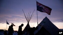 FILE - Travelers arrive at the Oceti Sakowin camp where people have gathered to protest the Dakota Access oil pipeline as they walk into a tent next to an upside-down American flag in Cannon Ball, North Dakota, Dec. 2, 2016. Some Native Americans worry the transition to a Donald Trump administration signals an end to eight years of land management reforms. But Trump's Native American supporters say they're hopeful he will cut through some of the government red tape that they believe has stifled economic progress on reservations.