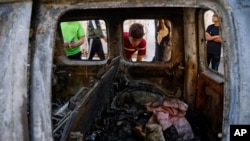 Palestinian kids look at a destroyed car after it was hit in an Israeli airstrike, in Gaza City, May 19, 2021.