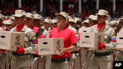FILE - Bolivarian militiamen hold boxes of subsidized food for distribution under a government program during an Independence Day parade in Caracas, Venezuela, July 5, 2019. Government revenue available to import food and medicine has long been scarce.