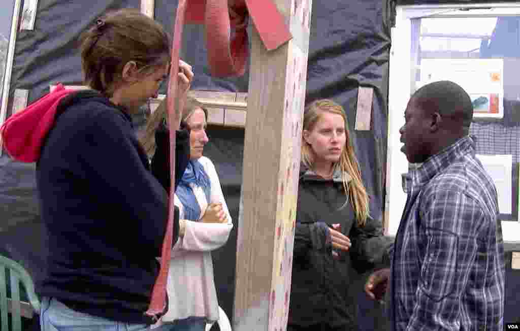 Nigerian Zimako Jones (R), who founded a migrant school at the Jungle camp, talks with volunteer teachers. (L. Bryant/VOA)