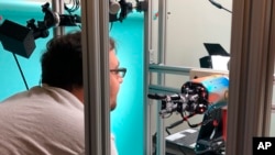 In this Thursday, July 26, 2018, photo, OpenAI researcher Jonas Schneider examines the research lab’s robotic hand in San Francisco. The hand, called Dactyl, has a single job, and that’s to rotate a cube until the letter facing up matches a random selection. (AP Photo/Ryan Nakashima)