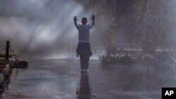 FILE - An opposition MDC party supporter hold his hands up after being sprayed with a water canon and in clouds of teargas on a street in Harare during clashes with police, Aug. 1, 2018.