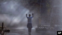 FILE - An opposition MDC party supporter hold his hands up after being sprayed with a water canon and in clouds of teargas on a street in Harare during clashes with police, Aug. 1, 2018.