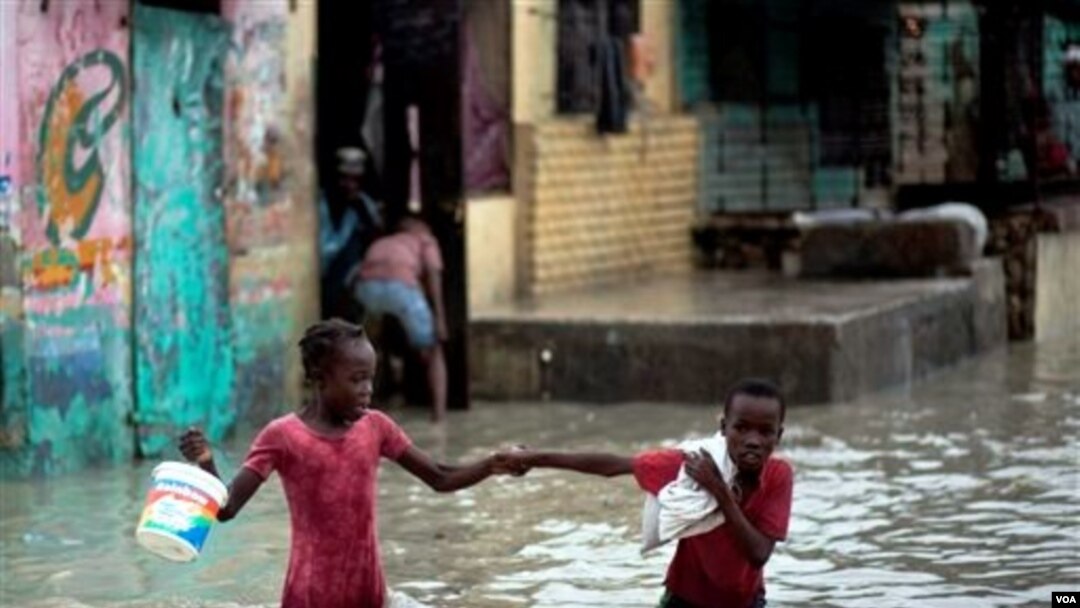 2 anak berjalan dalam air akibat banjir di Haiti, di khawatirkan penyakit Kolera yang menyebar ke luar daerah Artibonite berasal dari air.